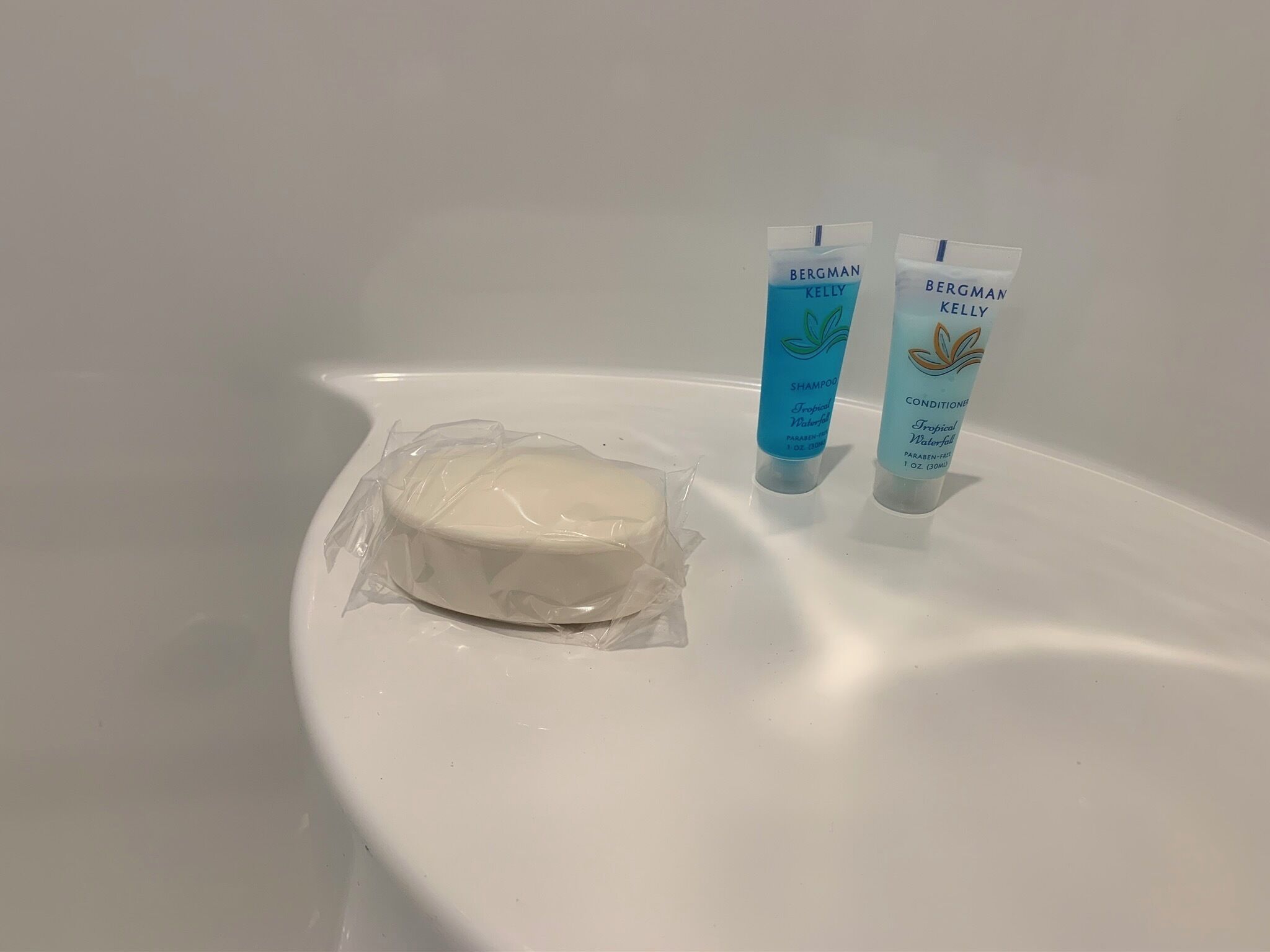 A bathroom with a white bathtub containing a bar of soap and two bottles of Bergman Kelly shampoo and conditioner.