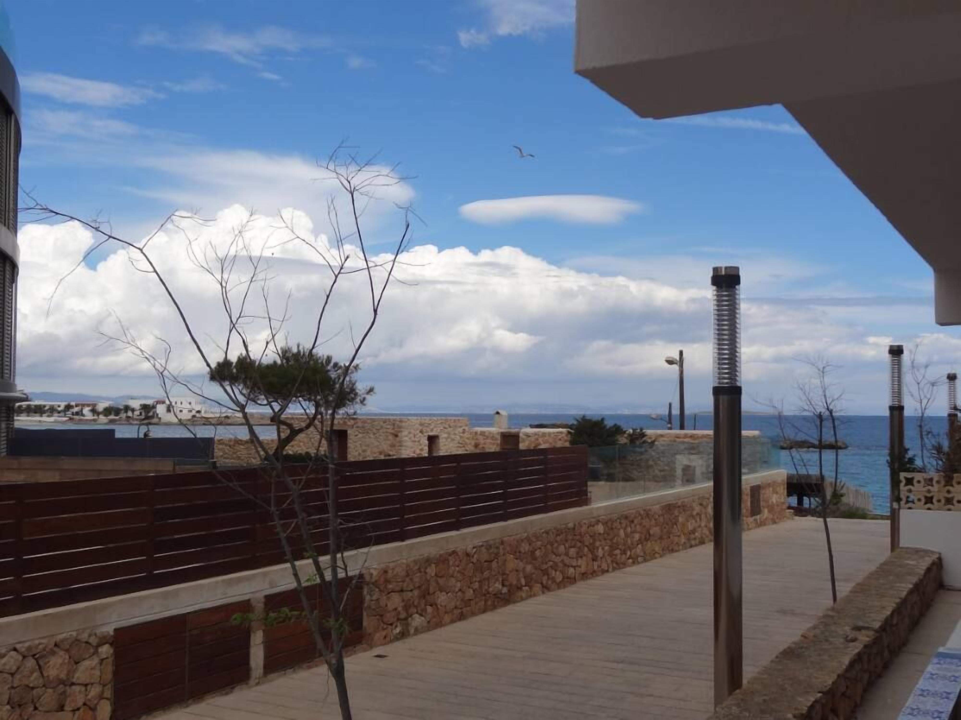 Une promenade en bord de mer, bordée de murs en pierre et de rampes en bois, qui mène à un point de vue sur la mer et les bâtiments situés au loin.