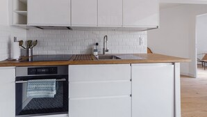 Une cuisine moderne avec des meubles blancs, un plan de travail en bois, un four encastré et un évier.