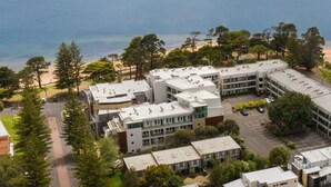 An aerial view of a coastal building complex with multiple units, surrounded by trees and a beach. - Sunrise Ocean Views Retreat Cowes Phillip Island (Cowes)