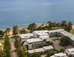An aerial view of a coastal building complex with multiple units, surrounded by trees and a beach. - Sunrise Ocean Views Retreat Cowes Phillip Island (Cowes)