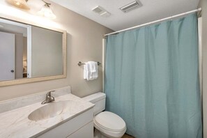 Ein Badezimmer mit Marmorwaschbecken, Toilette, Duschvorhang und Spiegel.
