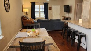 Un espacio habitable compacto con zona de comedor, sofá, televisor y encimera de cocina.