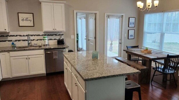 Una cocina con armarios blancos, encimera de granito y comedor con mesa y sillas.