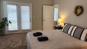 Un dormitorio con cama, mesita de noche, lámpara, puerta y un adorno en la pared.