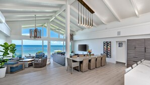 Amplia sala de estar con un gran ventanal con vista al océano, una mesa de comedor y una cocina moderna con televisor de pantalla plana.