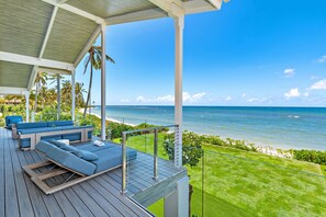 Relax in a serene oceanfront setting with unobstructed views, surrounded by lush tropical plants and a manicured lawn.