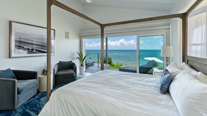 Un dormitorio moderno con una cama grande, vista al océano y un balcón con asientos.