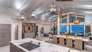 Una cocina moderna con una isla de mármol, iluminación colgante y vista al océano.