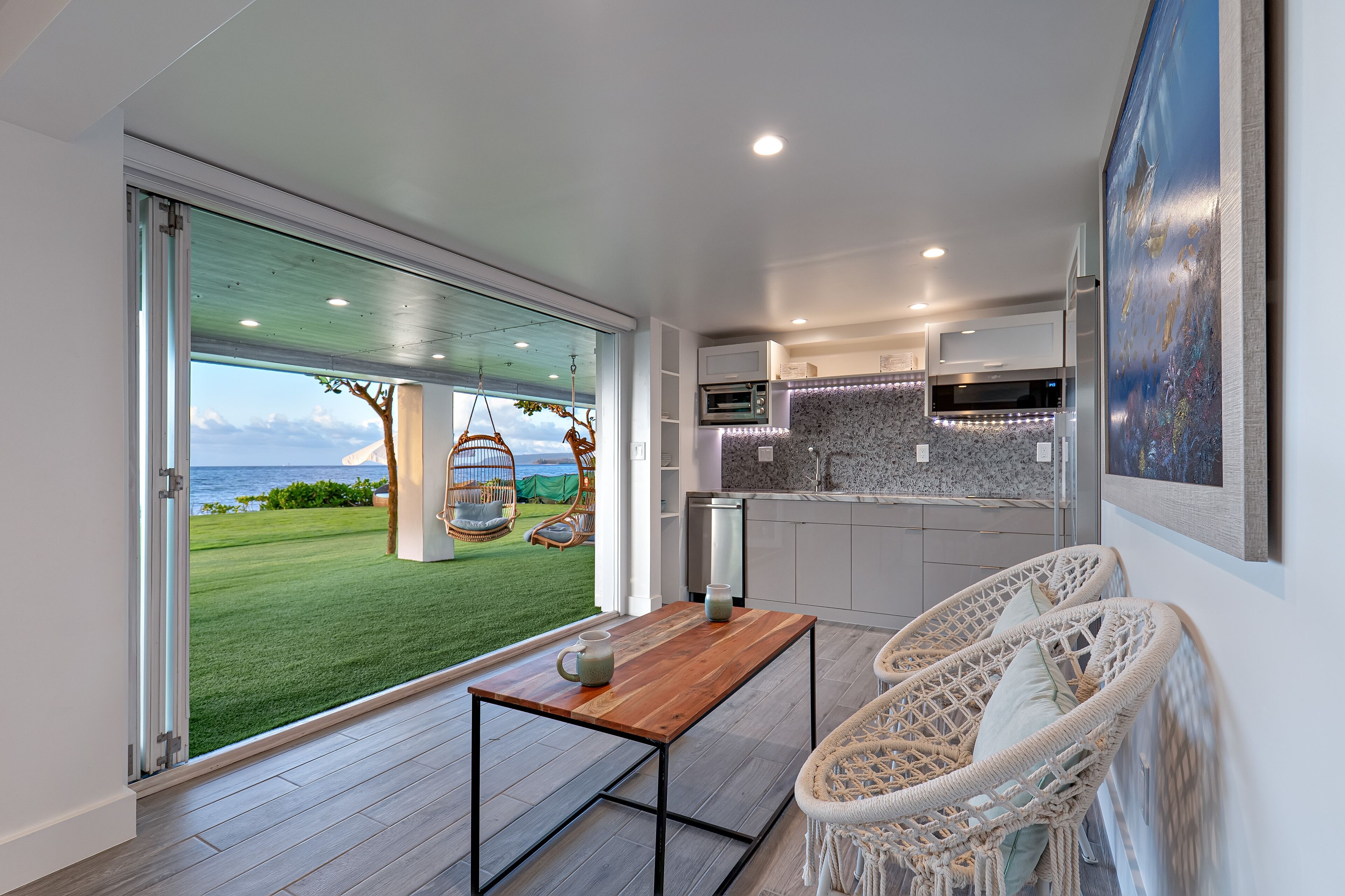 A modern kitchen with a large island, a dining area with a table and chairs, and a view of the ocean through a sliding glass door.
