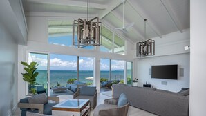 Un salón amplio con un gran ventanal con vistas al mar, un televisor de pantalla plana en la pared y un ventilador de techo.
