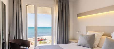 Een hotelkamer met een bed, een stoel, een nachtkastje en uitzicht op het strand door een schuifdeur.
