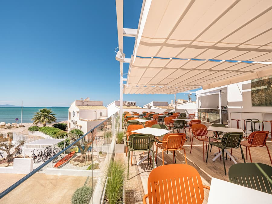 Una terraza con asientos al aire libre, vista al mar y un edificio de fachada blanca.
