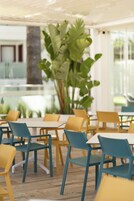 Un comedor con mesas y sillas, una planta grande y vistas al exterior.