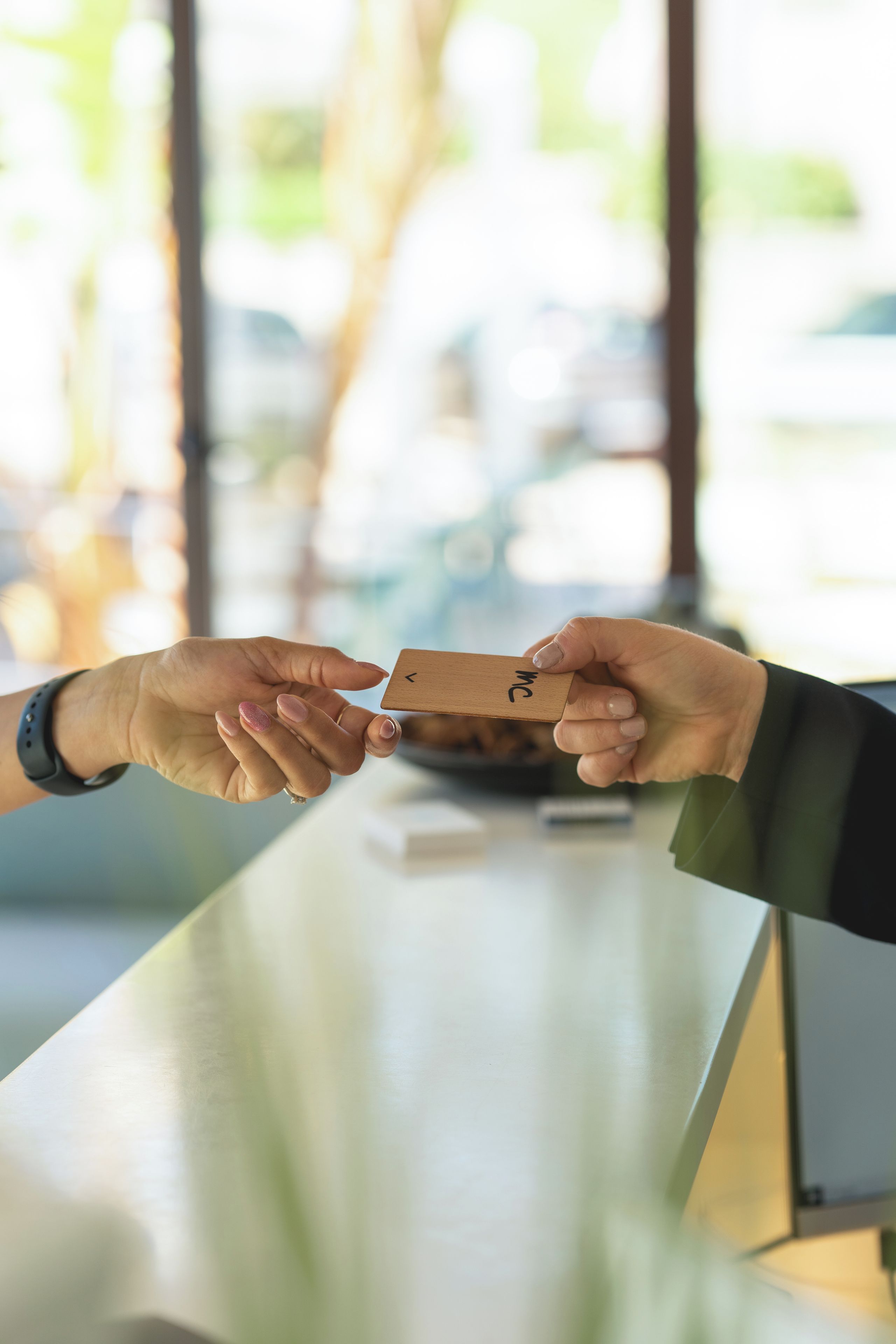 A hand holding a wooden card with "MC" written on it, being handed over at a counter.