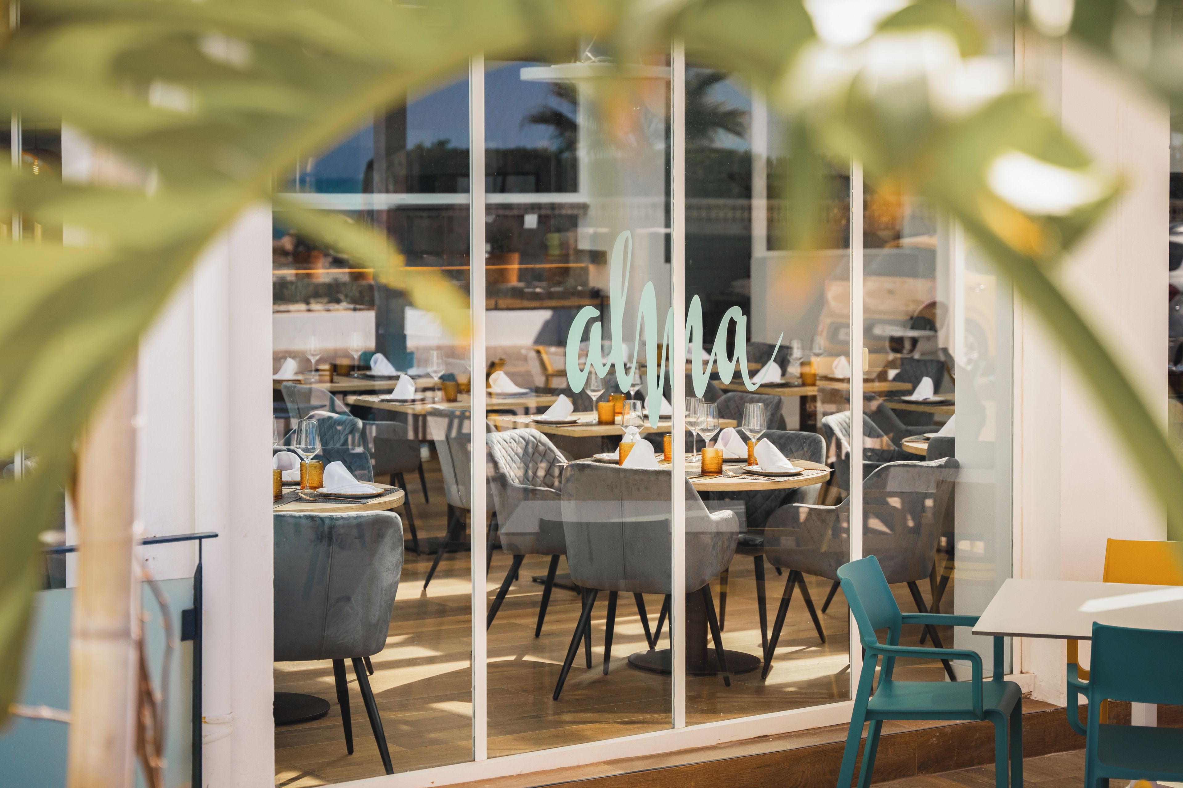 A restaurant with a glass wall, teal chairs, and a neon sign reading "ahima".