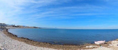 Une plage de galets avec un bateau et un ciel bleu clair.
