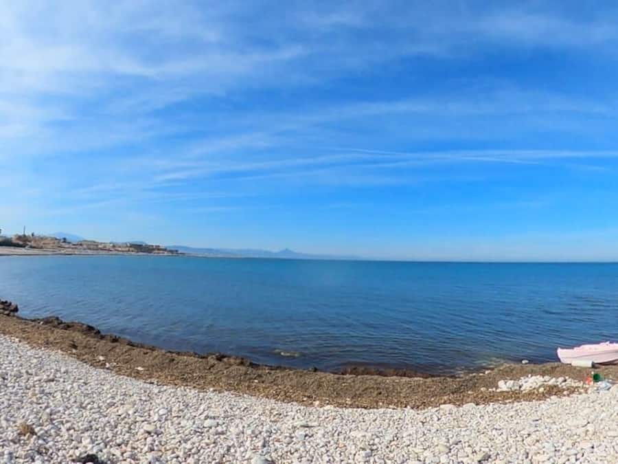 Una playa de guijarros con un bote y un cielo azul despejado.