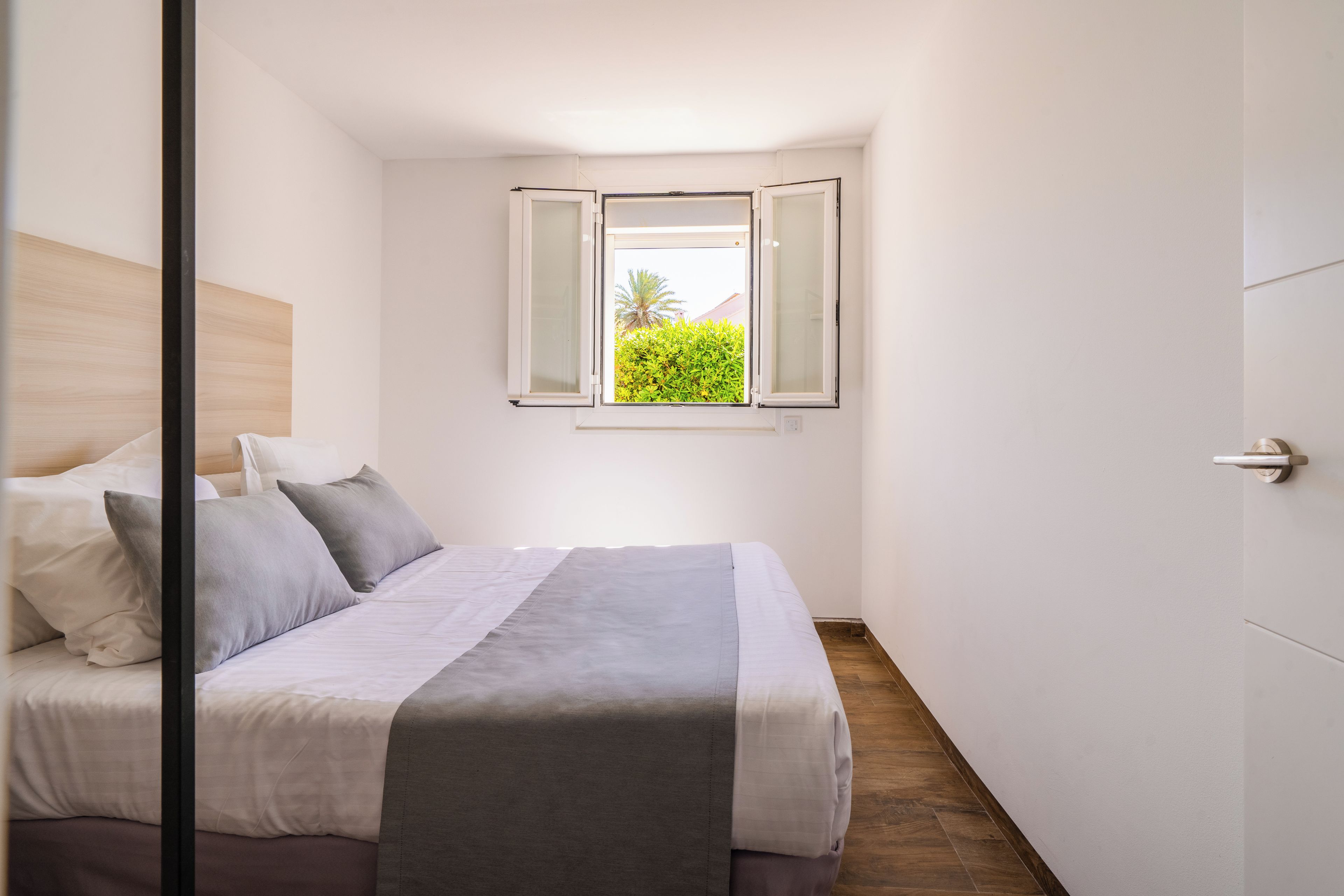 Un dormitorio con cama, una ventana con contraventanas abiertas y vistas al verdor exterior.