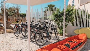 Un espacio cubierto con bicicletas estacionadas bajo una estructura blanca, un pequeño bote naranja y un edificio con fachada blanca y un letrero.