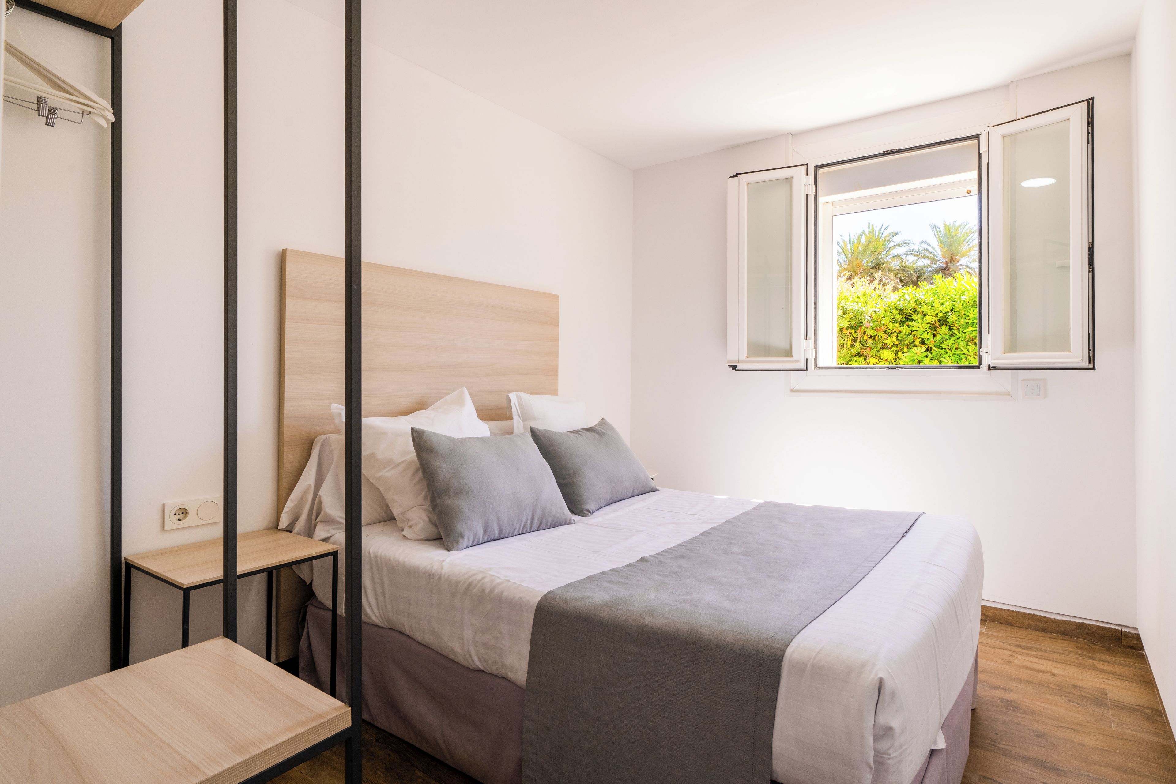 Un dormitorio con cama, mesitas de noche, un ventanal con vistas a zonas verdes y un enchufe en la pared.
