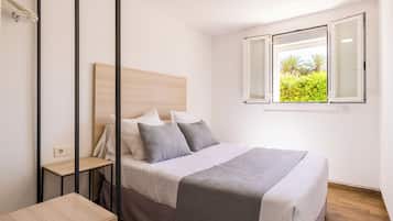 Un dormitorio con cama, mesitas de noche, un ventanal con vistas a zonas verdes y un enchufe en la pared.