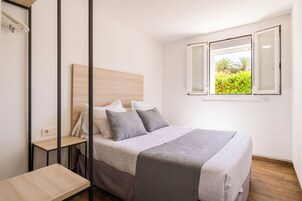 Un dormitorio con cama, mesitas de noche, un ventanal con vistas a zonas verdes y un enchufe en la pared.