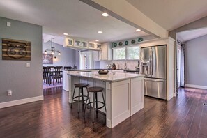 A modern kitchen with a central island, stainless steel appliances, and a dining area with a wooden table and chairs. - Spacious New Braunfels Escape w/ Private Deck! (New Braunfels)