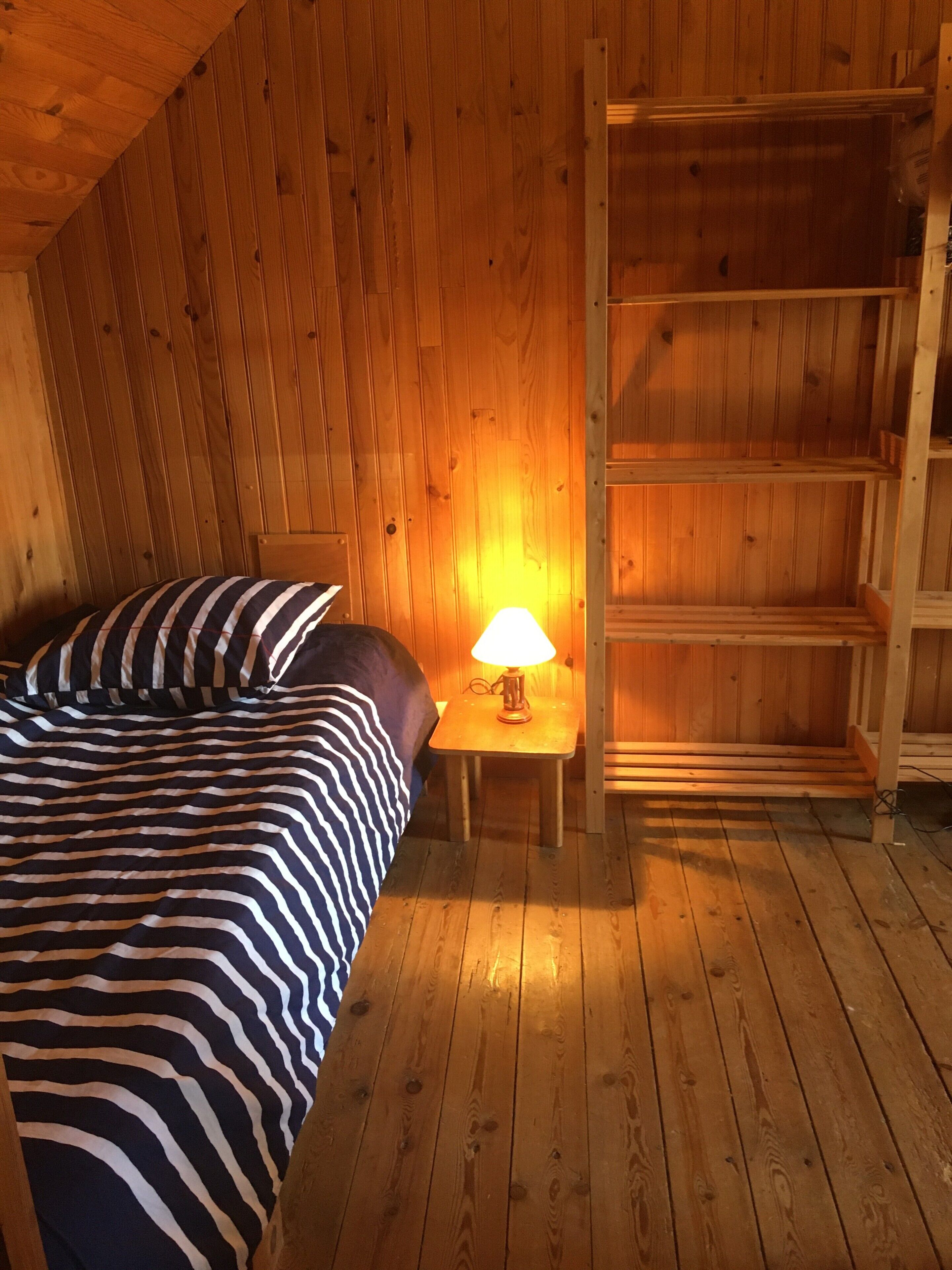 Une pièce en bois avec un lit, une table de chevet avec une lampe et une échelle en bois.