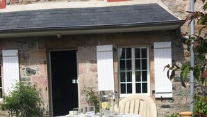 Ein Steinhaus mit einer schwarzen Tür, einem weißen Fenster mit Fensterläden und einem runden Tisch mit Stühlen.