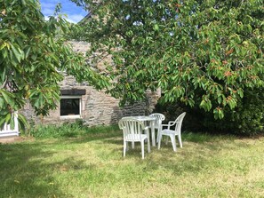A stone building with a window, surrounded by lush greenery and a tree with red fruits. - Charming Little House in the Meadow for 4–5 Guests (plurien)