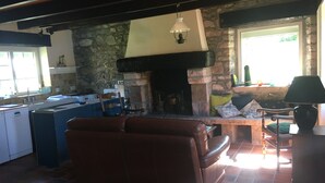 Ein gemütliches Wohnzimmer mit Kamin aus Stein, einer Couch und einer Küchenzeile mit Fenster.