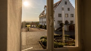Vista a través de una ventana que muestra un patio interior con una fuente y una escalera que lleva a la entrada.
