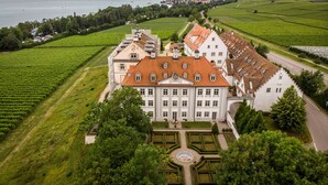 Un edificio grande e histórico con fachada simétrica, rodeado de jardines cuidados y viñedos.