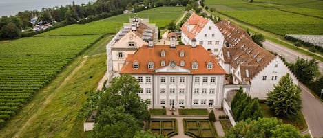 A large, historic building with a symmetrical facade, surrounded by well-maintained gardens and vineyards.