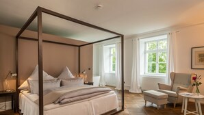 Una cama con dosel, una mesita de noche, una silla, una pequeña mesa y una ventana con cortinas.