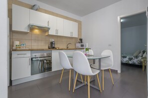 Une cuisine moderne avec des meubles blancs, un four à micro-ondes, une machine à café et une table à manger avec quatre chaises.