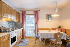 A kitchen with wooden cabinets, a stove, and a dining area with a table and chairs. - Holiday Apartment "3 - Ciasa Primula" (san Vigilio di Marebbe)