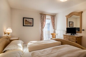 A hotel room with two beds, a television, a mirror, a lamp, and a window with curtains. - Holiday Apartment "3 - Ciasa Primula" (san Vigilio di Marebbe)