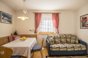 Una habitació acollidora amb una taula de dinar, un sofà blau, una finestra amb cortines i una làmpada penjant.