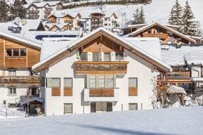 Un edifici cobert de neu amb un balcó, finestres de fusta i una pista d'esquí al fons.