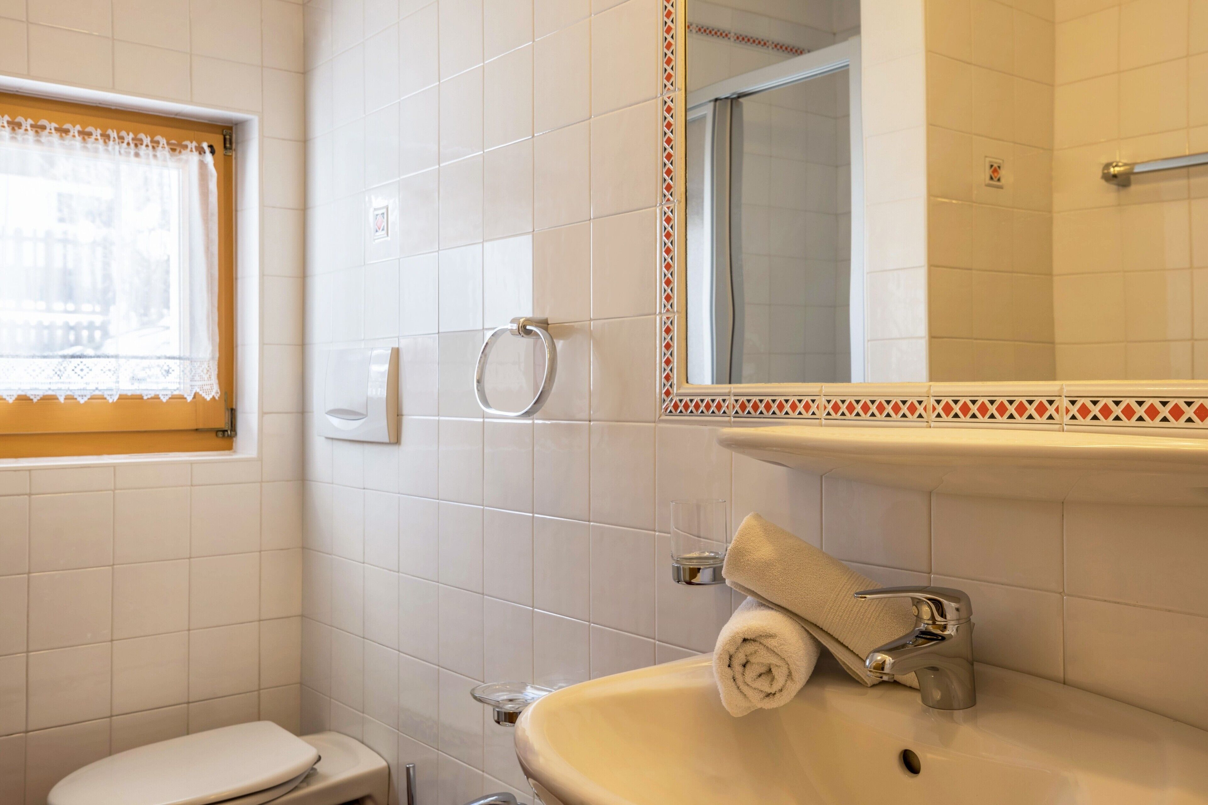 Ein Badezimmer mit Toilette, Waschbecken, Spiegel und Fenster mit Spitzenvorhängen.
