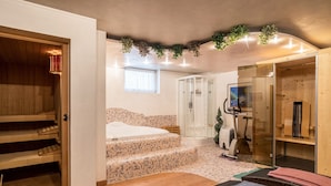 A spa room with a wooden bench, a massage table, a shower area, and a small staircase leading to a bed.
