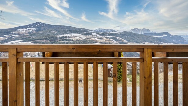 A wooden railing with a view of snow-covered mountains and a clear sky.