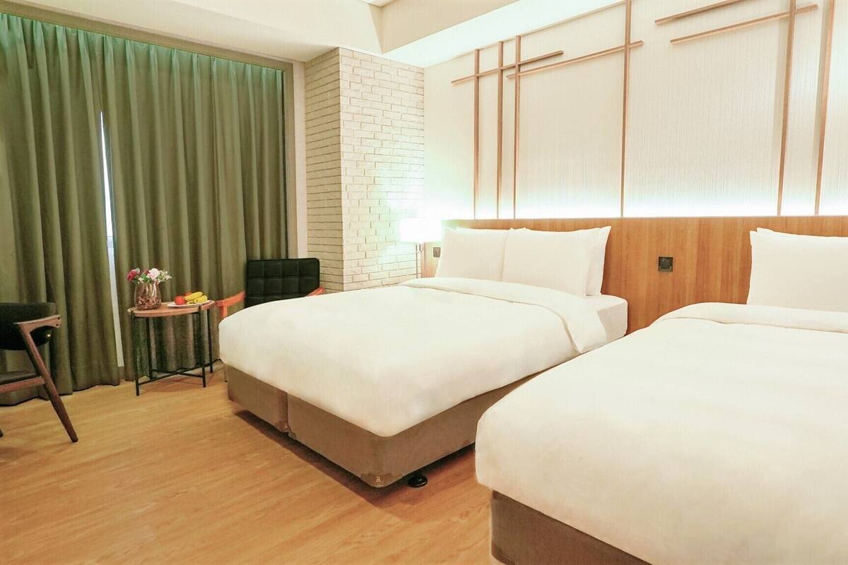 A hotel room with two beds, a desk, a chair, and a green curtain.