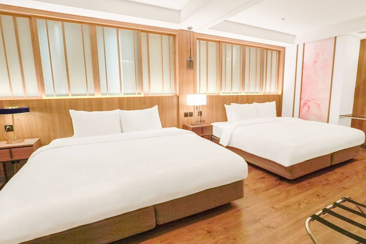 A hotel room with two beds, wooden paneling, a desk, and a chair.