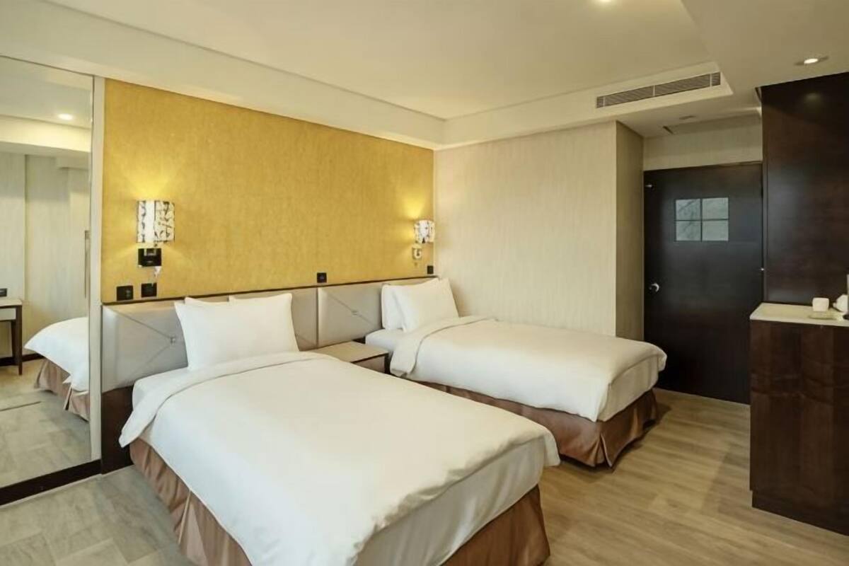A hotel room with two beds, a large mirror, a dark door, and a wooden cabinet.