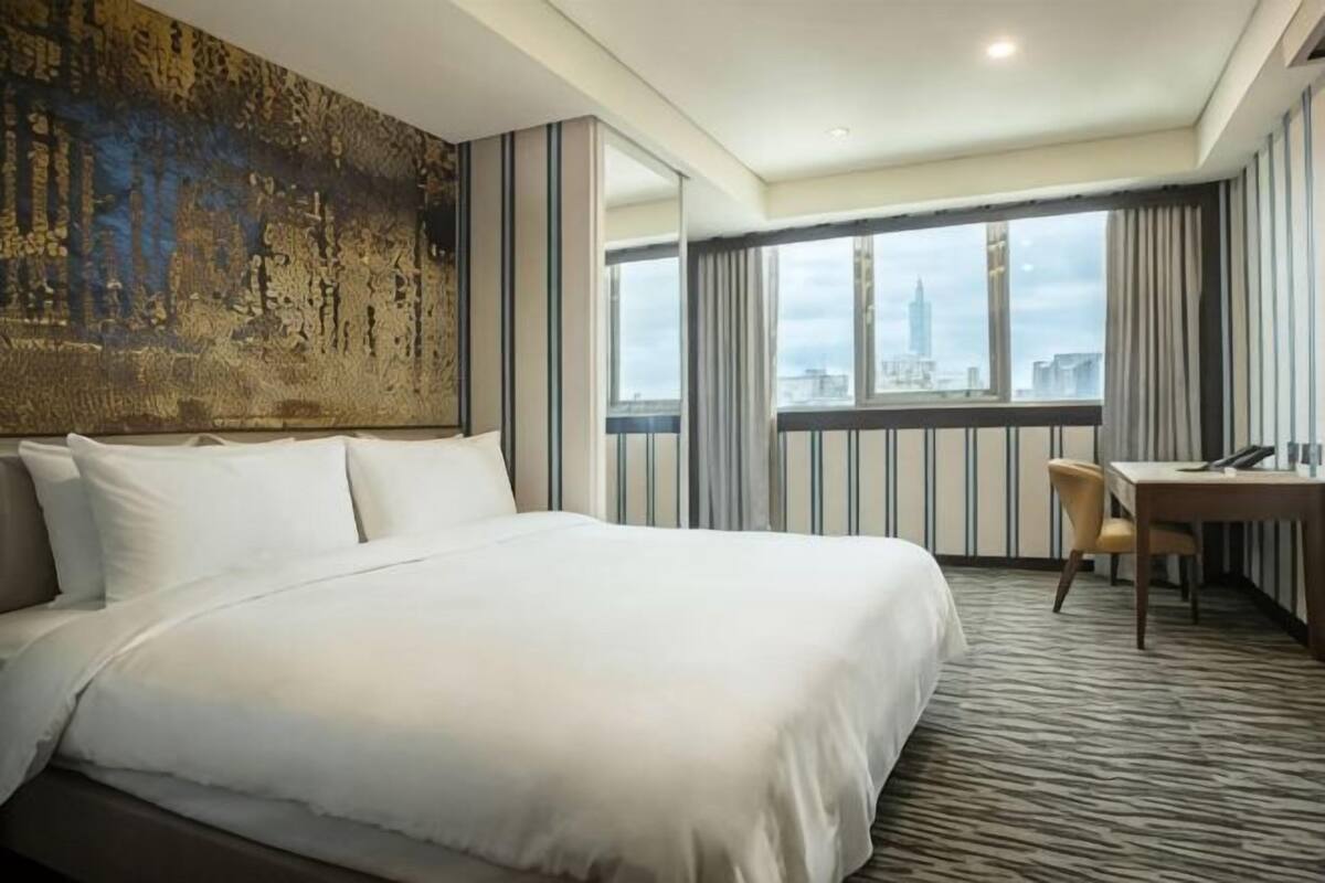 A hotel room with a large bed, a desk, a chair, and a view of the city.