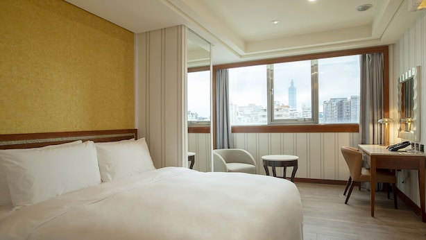 Une chambre d’hôtel avec un grand lit, un bureau, une chaise et une vue sur le paysage urbain.