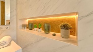 Un meuble-lavabo pour la salle de bain avec un plan de toilette en marbre, un miroir et une étagère ornée de plantes en pot et d’une bougie.